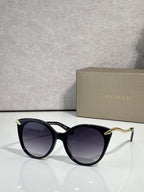 Sunglasses, black rounded frames with gold-tone temple tips and dark tinted lenses