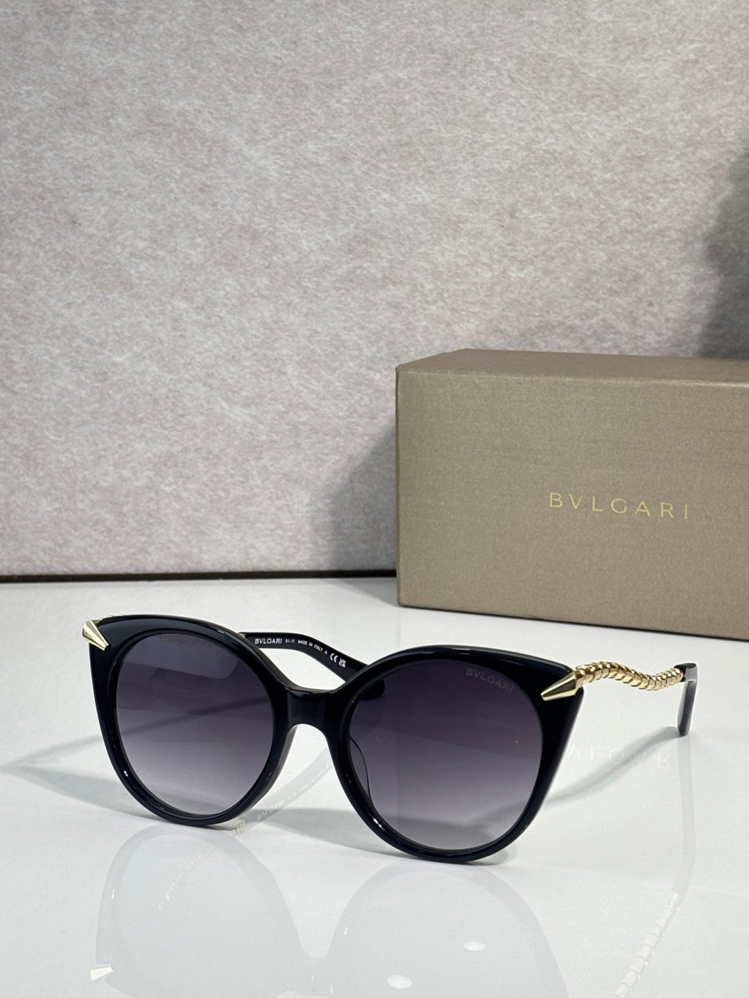 Sunglasses, black rounded frames with gold-tone temple tips and dark tinted lenses