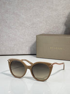 Sunglasses, tan rounded frames with gold-tone temple tips and dark tinted lenses