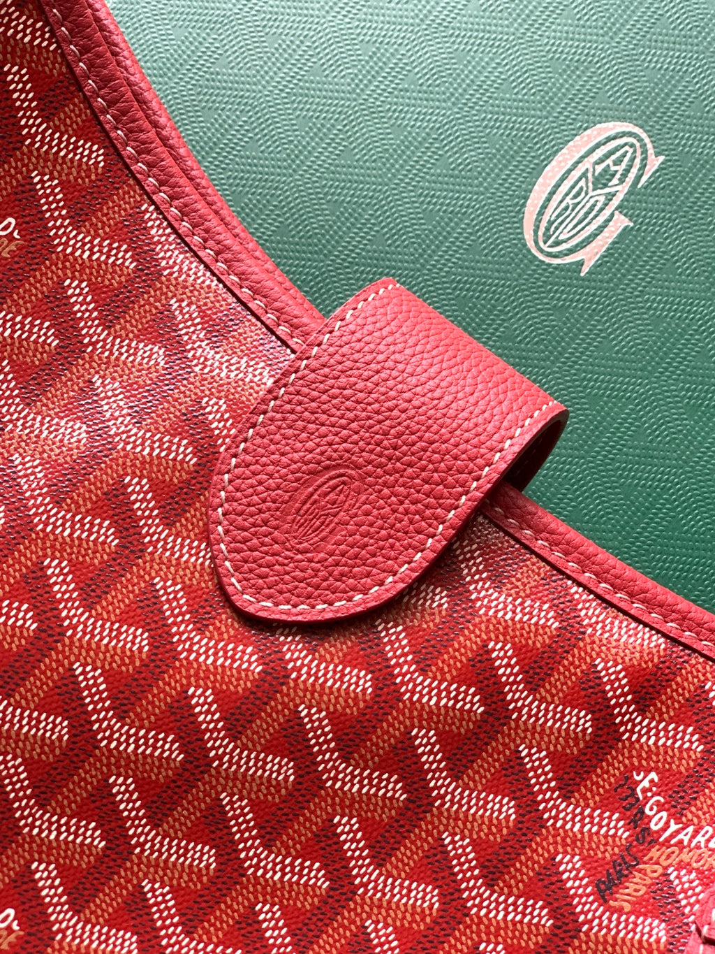 Red handbag corner with pebble-grain leather trim and embossed canvas surface