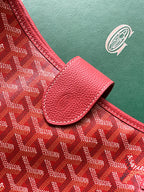 Red handbag corner with pebble-grain leather trim and embossed canvas surface