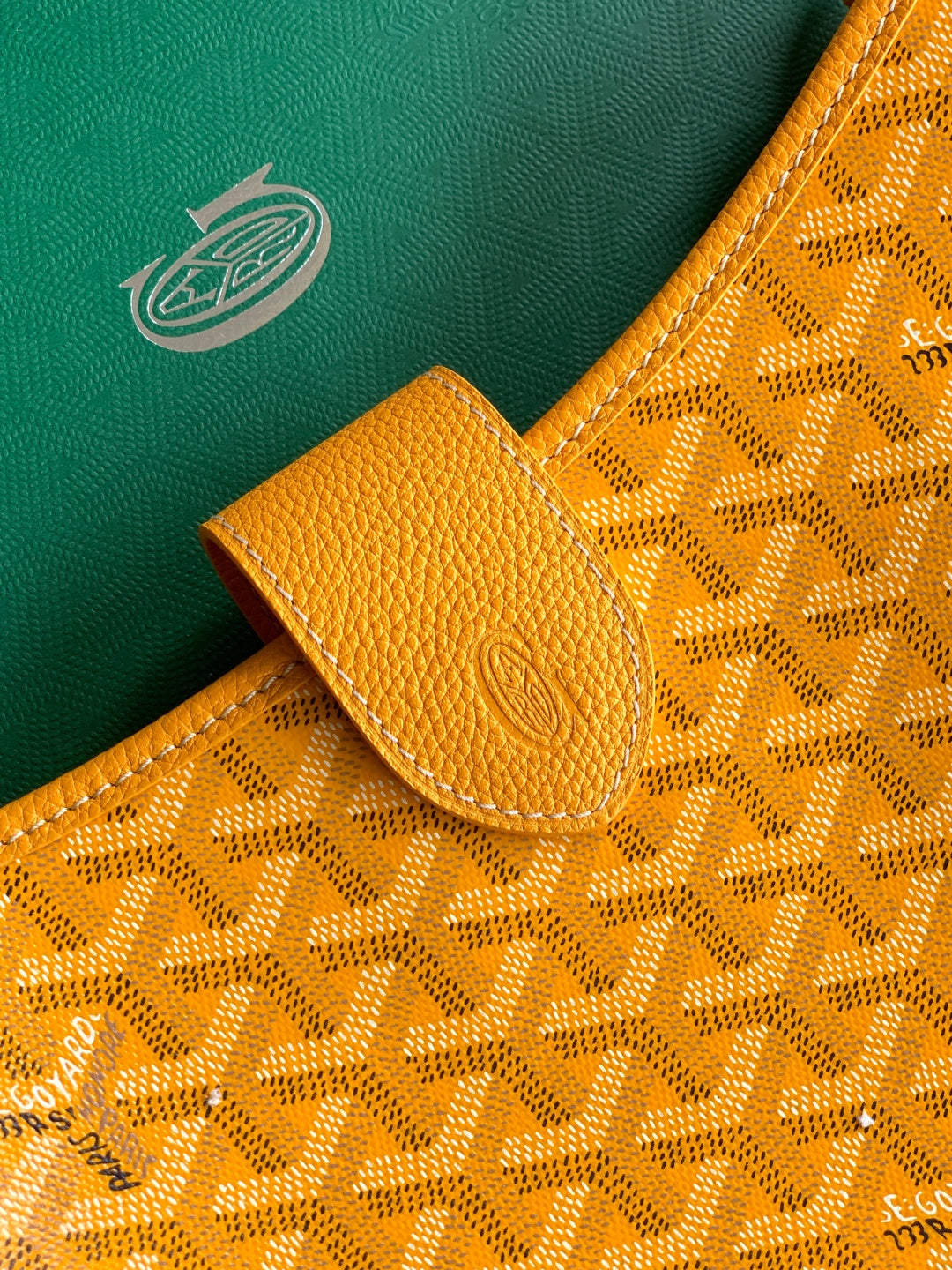 Close-up of mustard leather tab and embossed monogram fabric on the bag