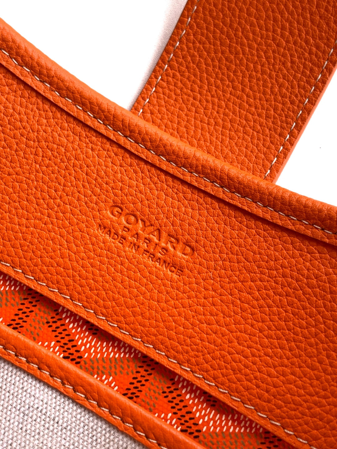 Orange leather bag trim with embossed logo text and double-stitched edge