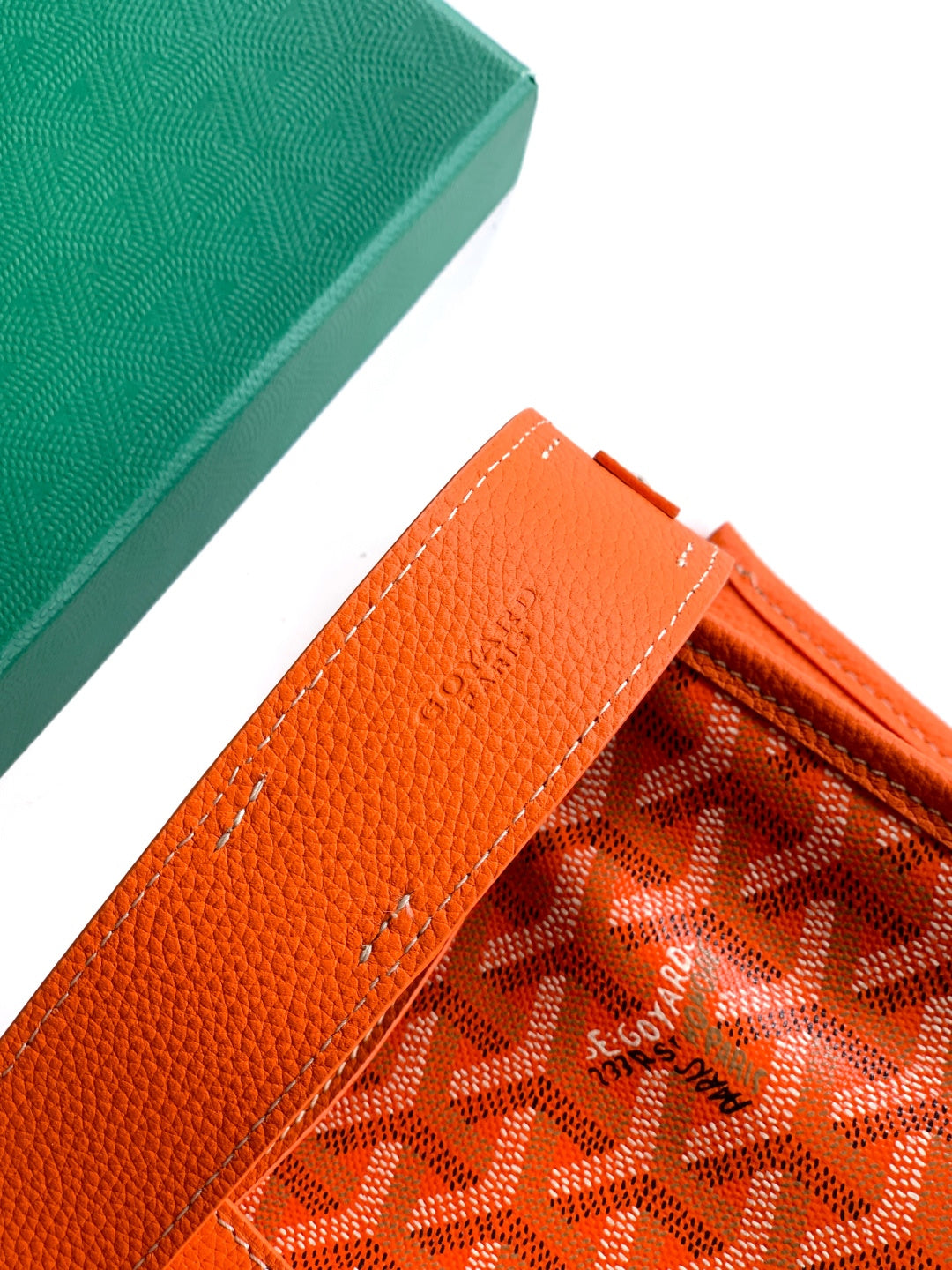 Orange leather strap detail on a monogram canvas bag with stitched lines