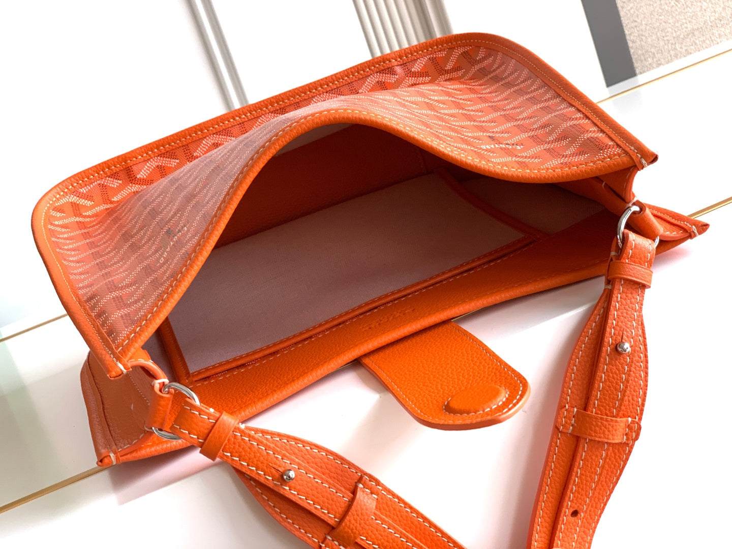 Orange monogram canvas bag open with leather interior, strap, and hanging strap tab