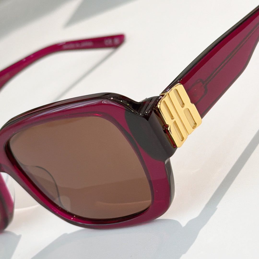 Maroon sunglasses close-up with tinted lens and gold bar bridge detail.