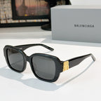 Sunglasses, black square frames with smoke lenses and gold bar accents.