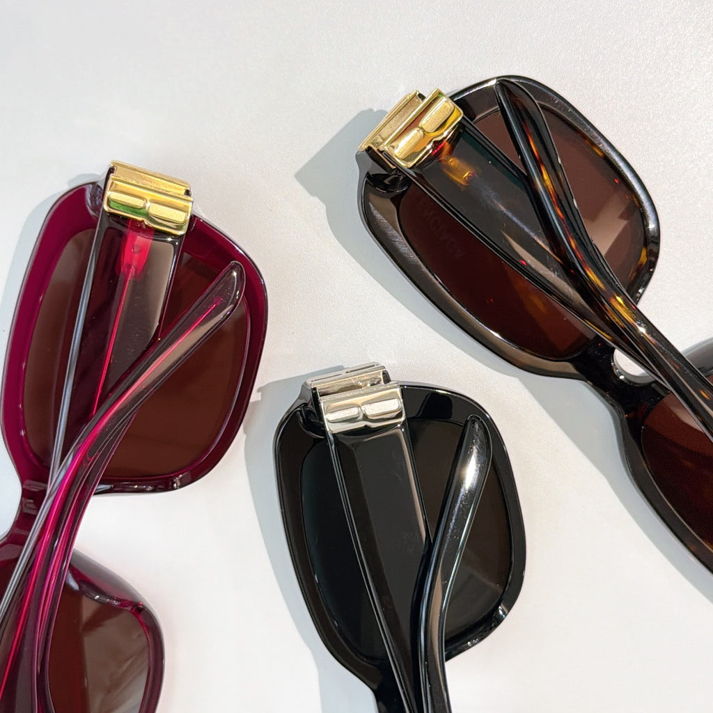 Assorted sunglasses close-up in burgundy and black with gold bar hinge details.