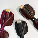Assorted sunglasses close-up in burgundy and black with gold bar hinge details.