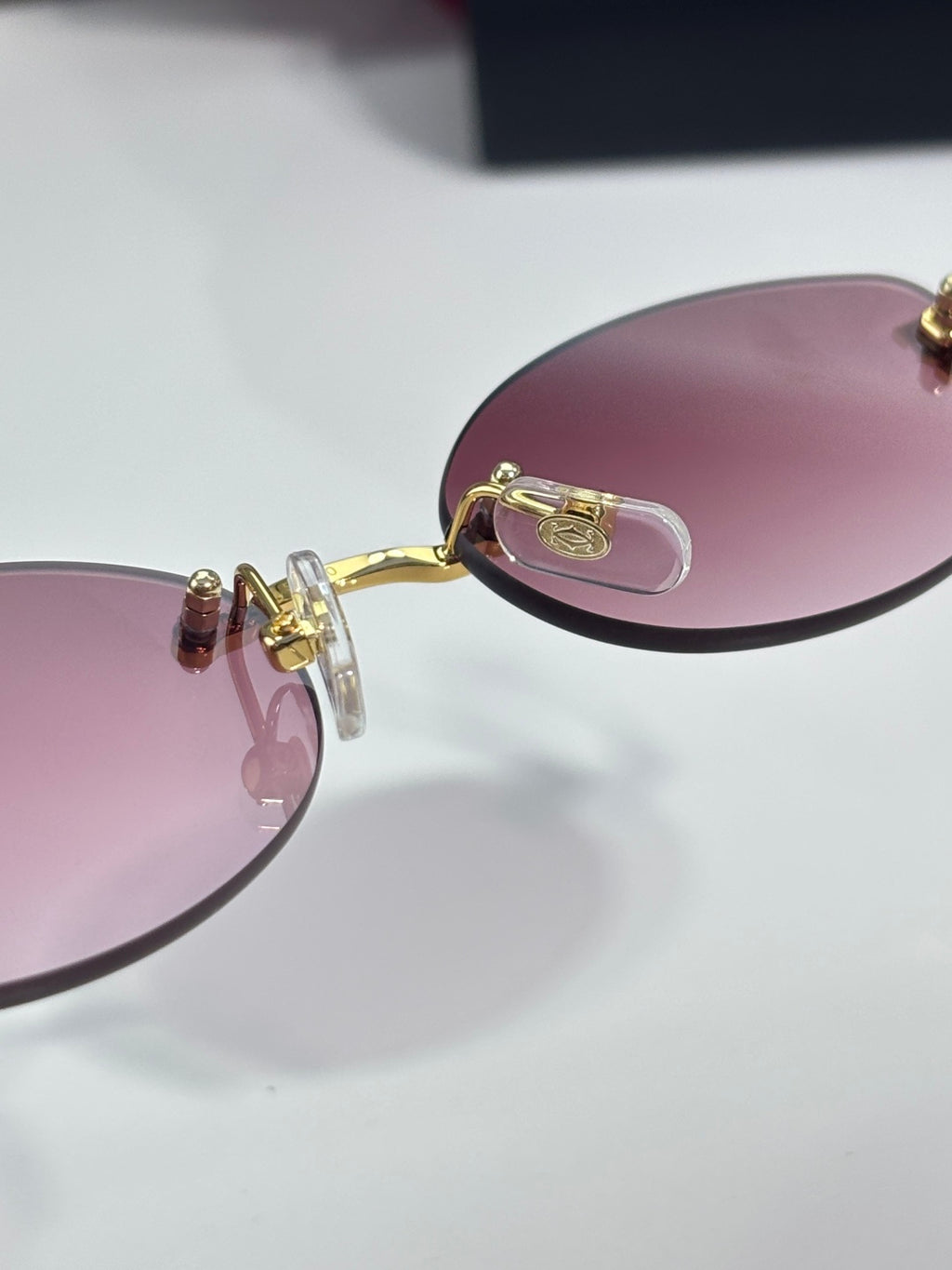 Close-up of round sunglasses frame with pink tinted lens and gold hinge detail