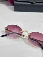 Round sunglasses close-up with pink tinted lenses, gold frame, and dark temples