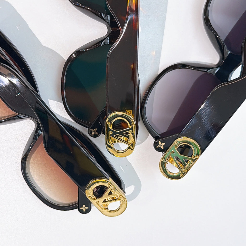 Black cat-eye sunglasses close-up with gold LV logos and teal/purple tinted lenses