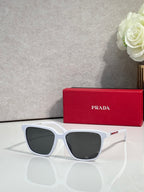 Prada sunglasses with white frames, red side accents, and dark lenses.