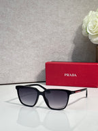 Prada sunglasses with black frames and red side accents, featuring dark lenses.