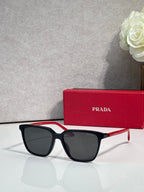 Prada sunglasses with black frames, red side accents, and dark lenses.