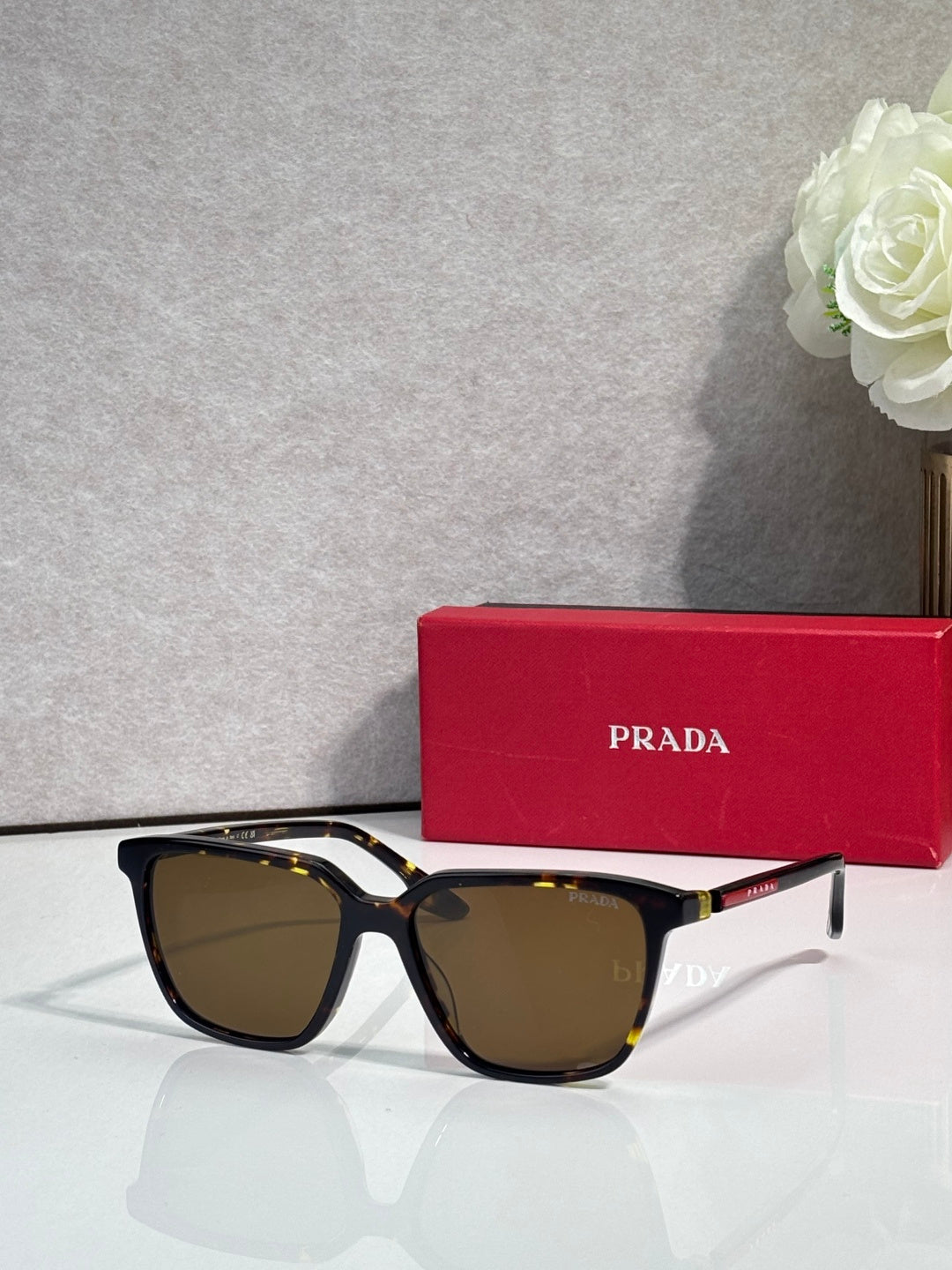 Prada sunglasses with dark tortoise-style frames, red side accents, and brown lenses.