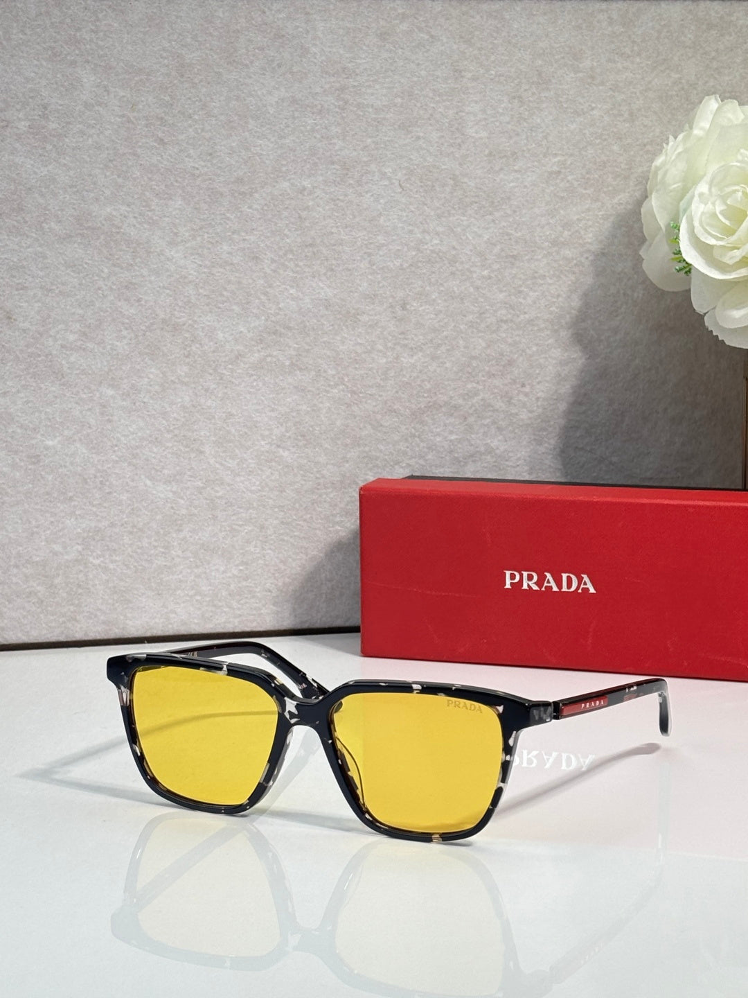 Prada sunglasses with black frames, red side accents, and yellow lenses.