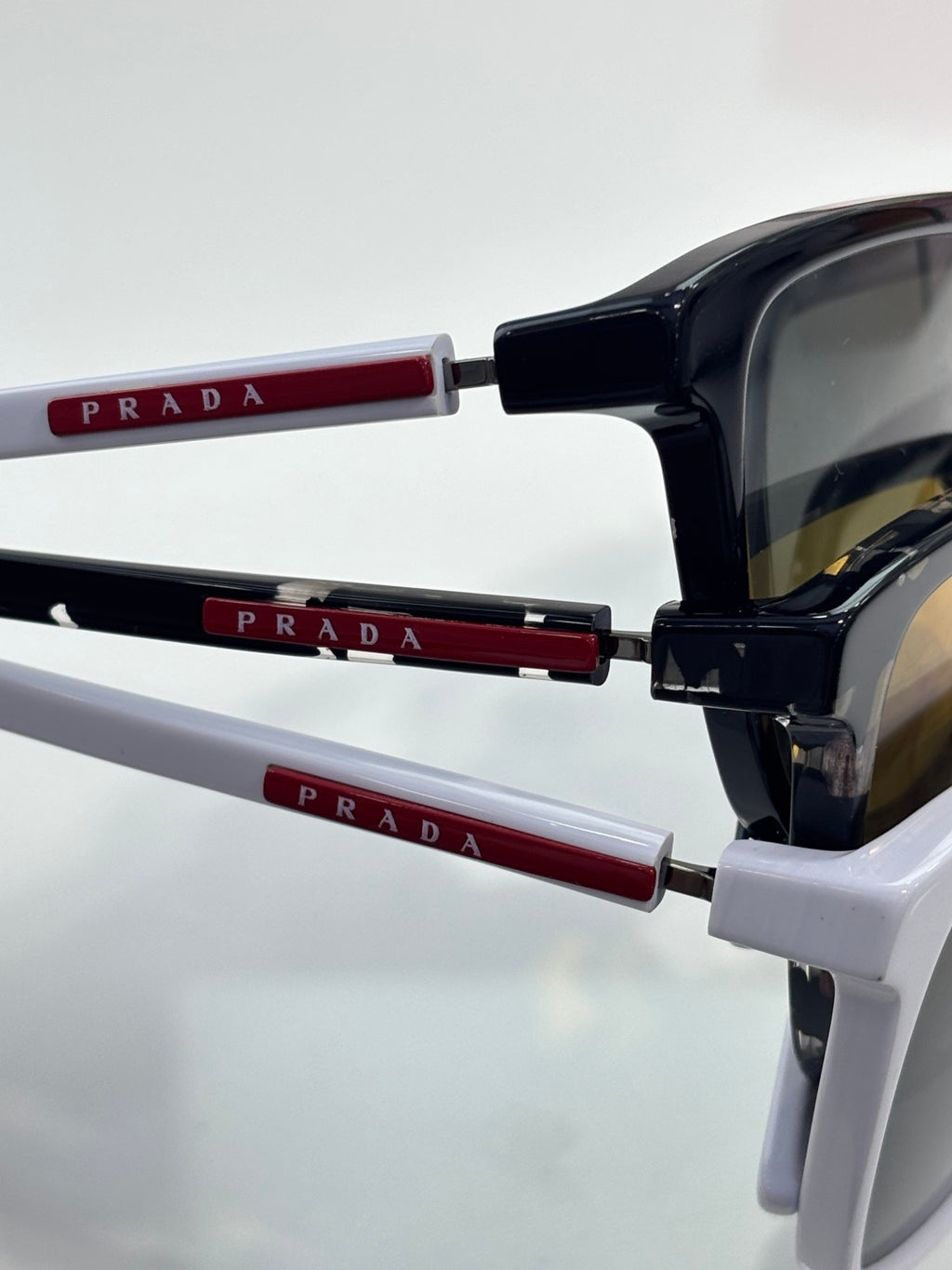 Prada sunglasses close-up: black frame with red temple details and dark lenses.