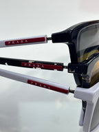 Prada sunglasses close-up: black frame with red temple details and dark lenses.