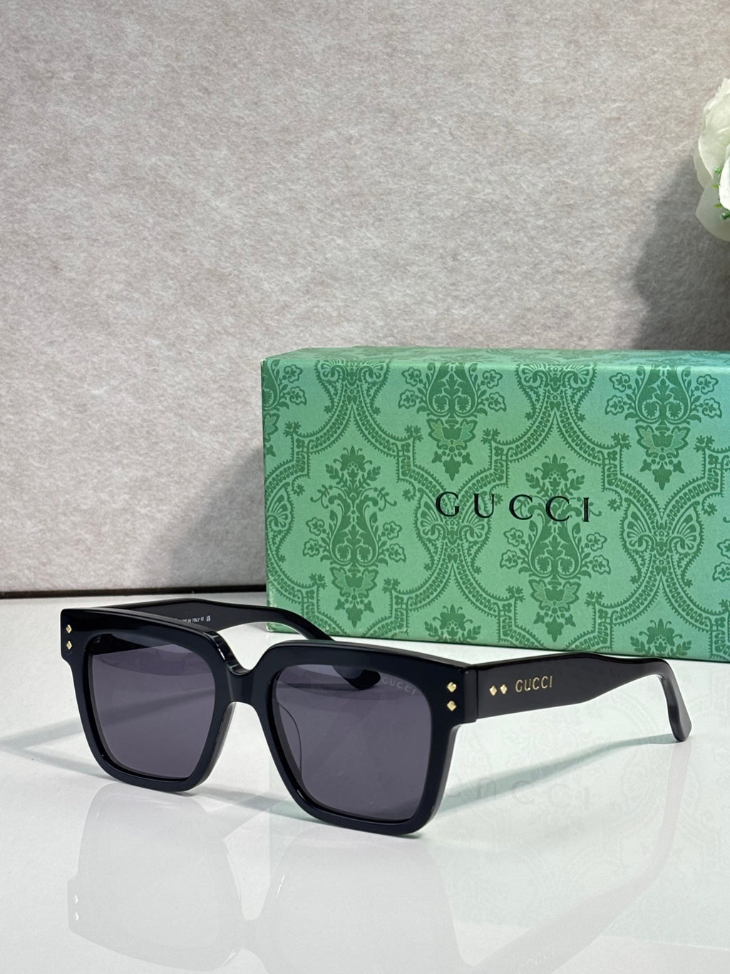 Gucci square sunglasses with dark lenses and black frame, gold stud accents on temples