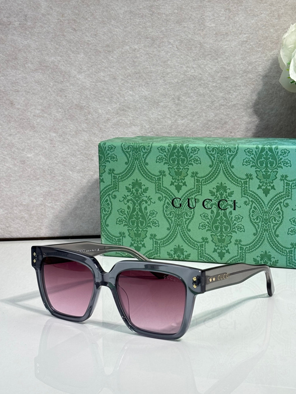 Gucci square sunglasses with pink-tinted lenses and black frame, gold stud accents on temples