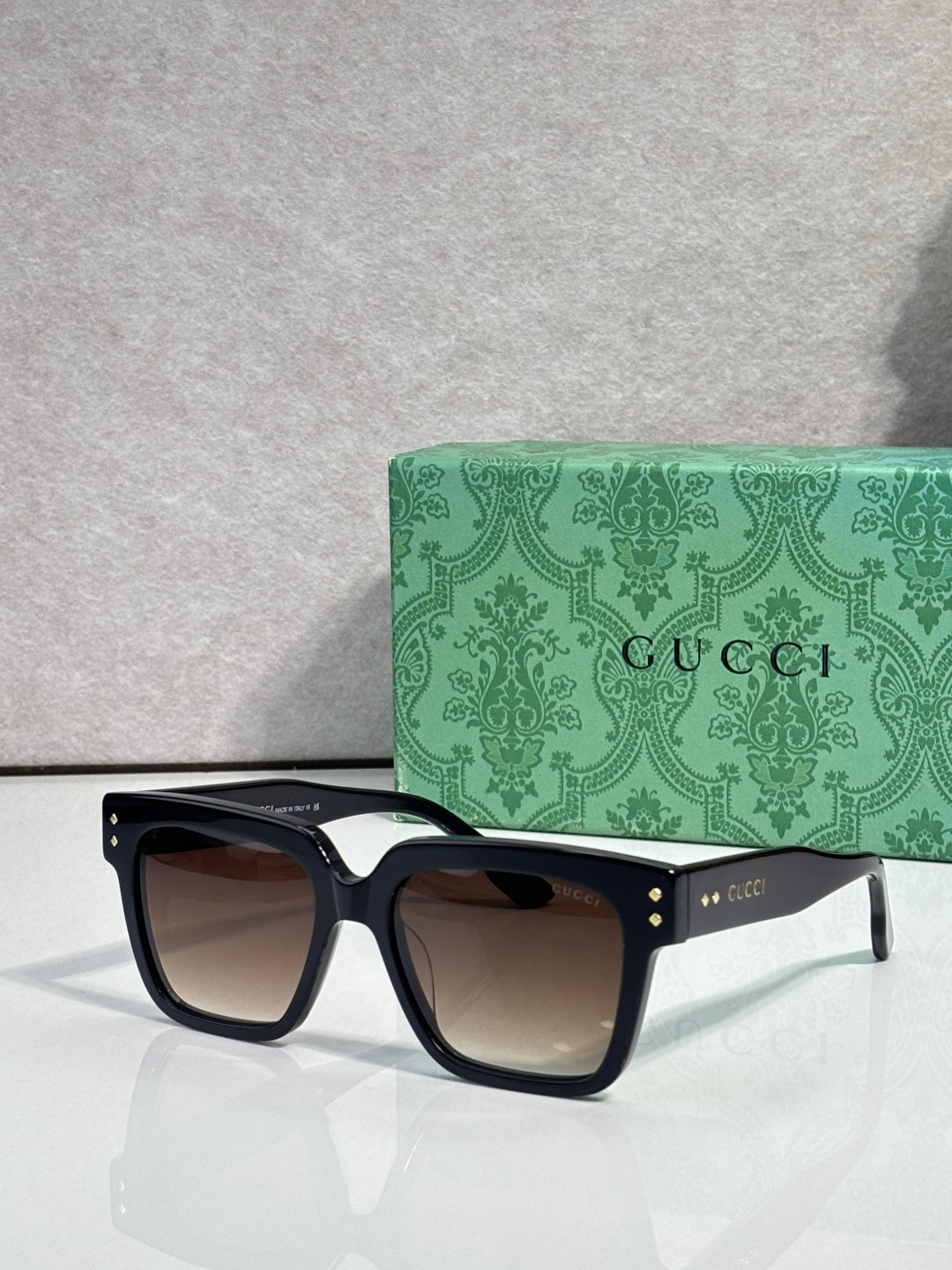 Gucci square sunglasses with dark lenses and black frame, gold detail studs on temple arms
