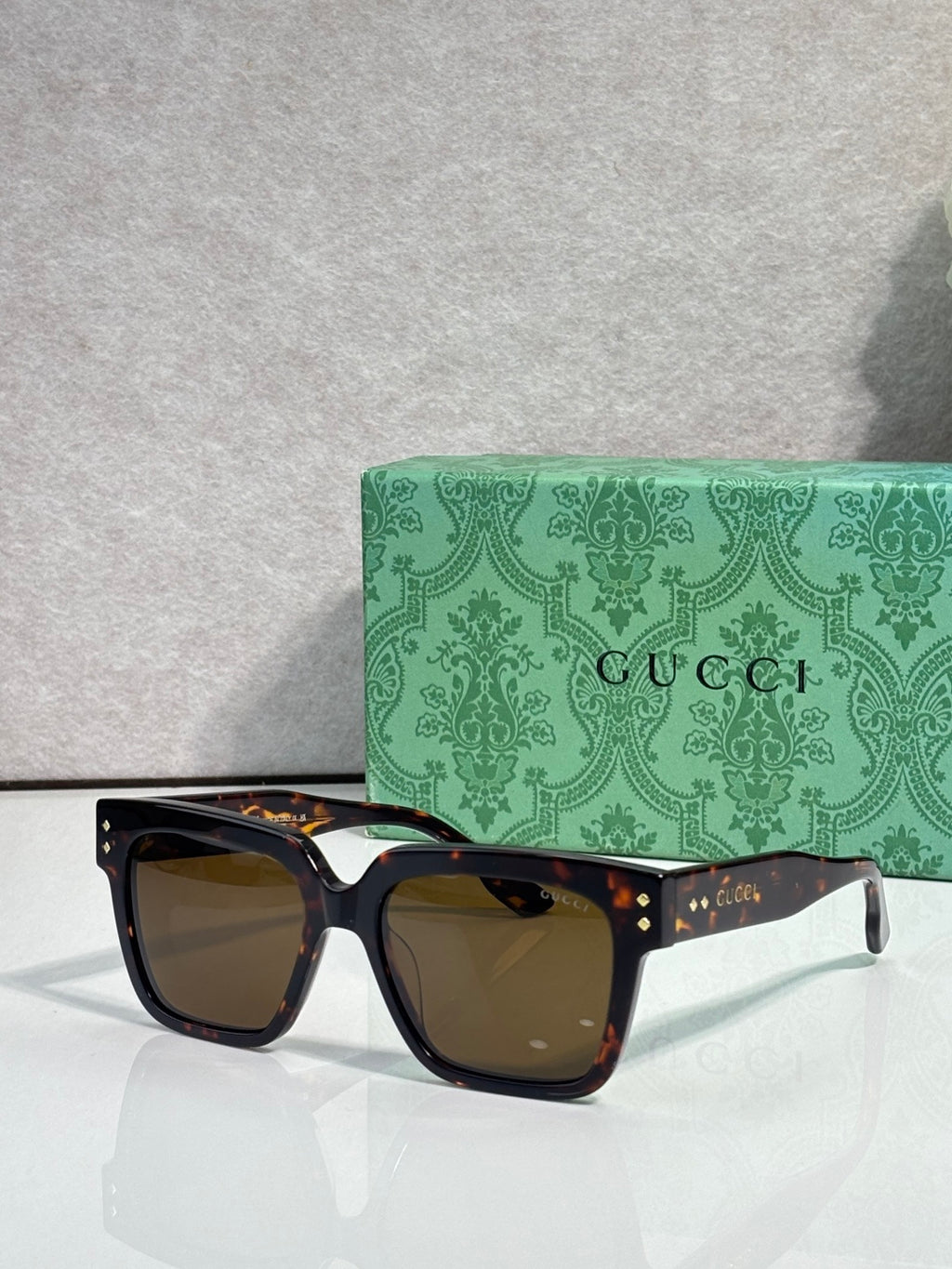 Gucci square sunglasses with brown-tinted lenses and black frame, gold studs on temples