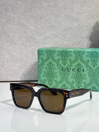 Gucci square sunglasses with brown-tinted lenses and black frame, gold studs on temples