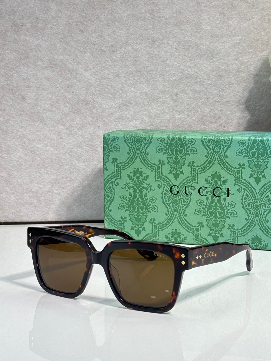 Gucci square sunglasses with brown-tinted lenses and black frame, gold studs on temples