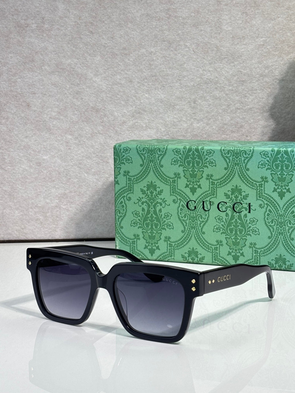 Gucci square sunglasses with dark lenses and black frame, front view with gold logo on temple