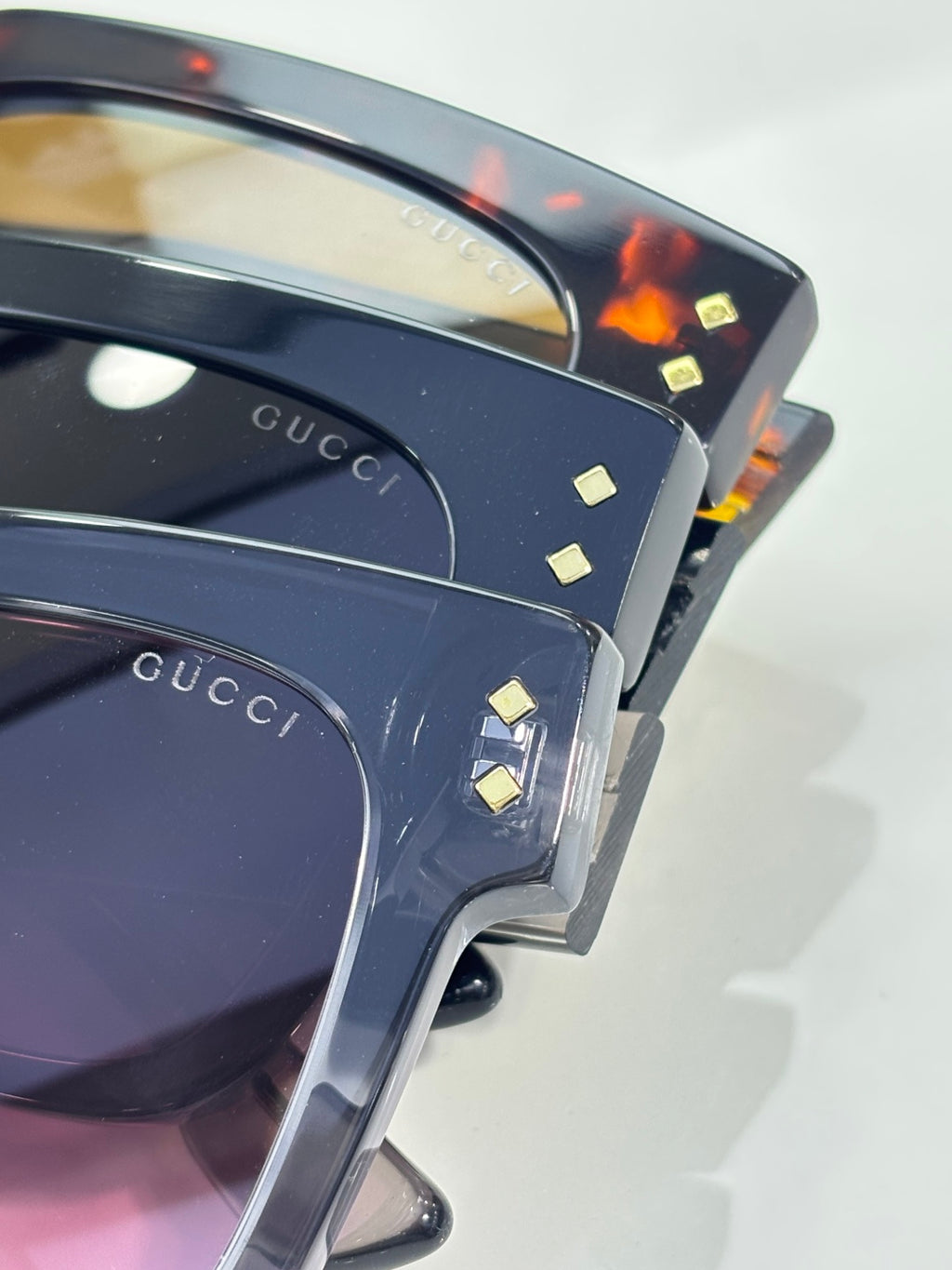 Gucci sunglasses close-up of dark blue frames with gold stud accents and pink lenses