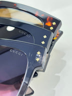 Gucci sunglasses close-up of dark blue frames with gold stud accents and pink lenses