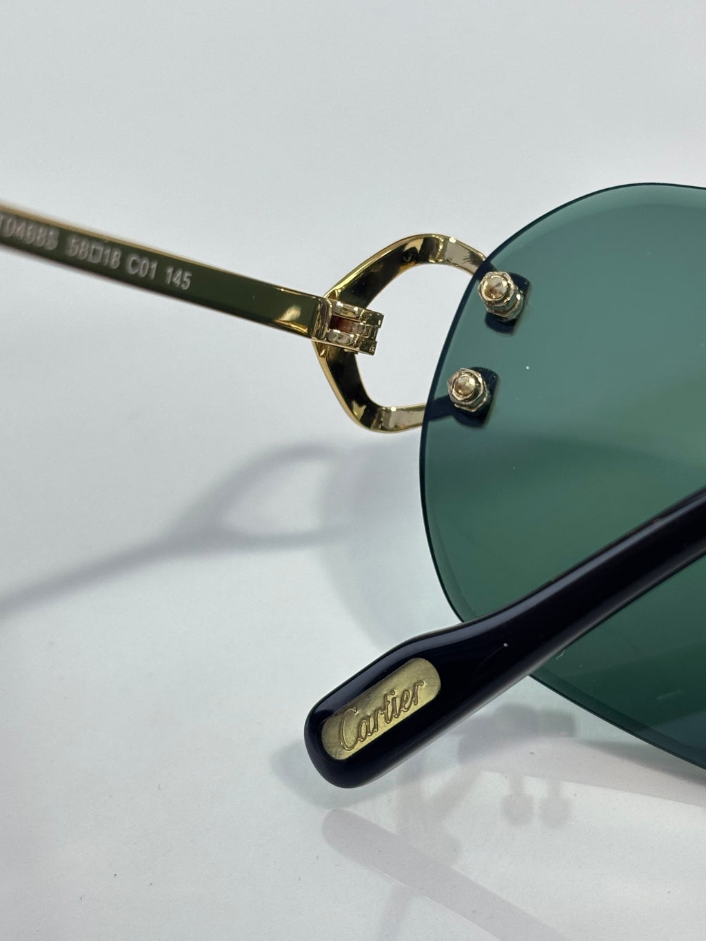 Close-up of Cartier sunglasses: green lens with gold hinge and black temple