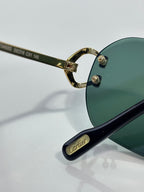 Close-up of Cartier sunglasses: green lens with gold hinge and black temple
