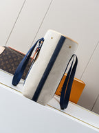 Beige canvas tote bag with navy side panels, long handles, and gold studs