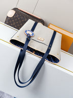 Beige canvas tote bag with navy strap accents, top opening, and gold-tone details