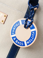 Beige canvas charm tag on navy strap with circular "THINK & BAGS" label