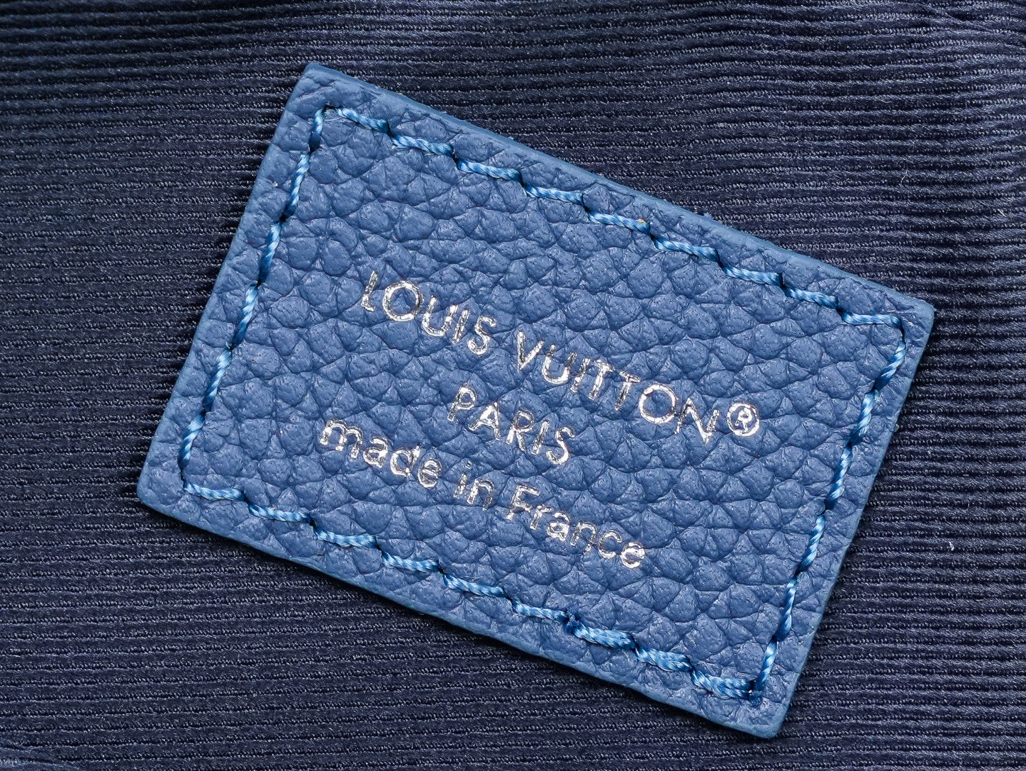 Blue leather brand label on crossbody bag with embossed text