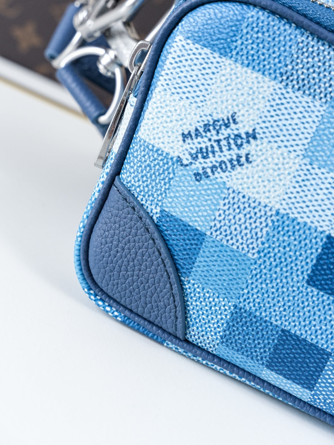 Blue check-pattern bag corner detail with smooth leather trim and stitching