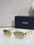 Sunglasses with light beige frames, gold logo accents, and amber tinted lenses