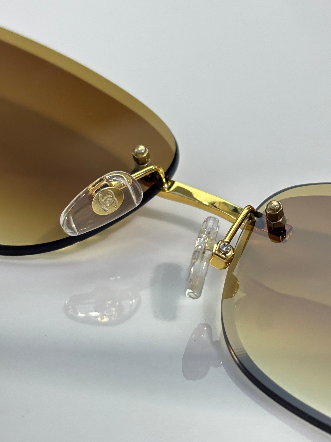 Close-up of gold sunglasses frame with dark lens rim and logo hinge detail