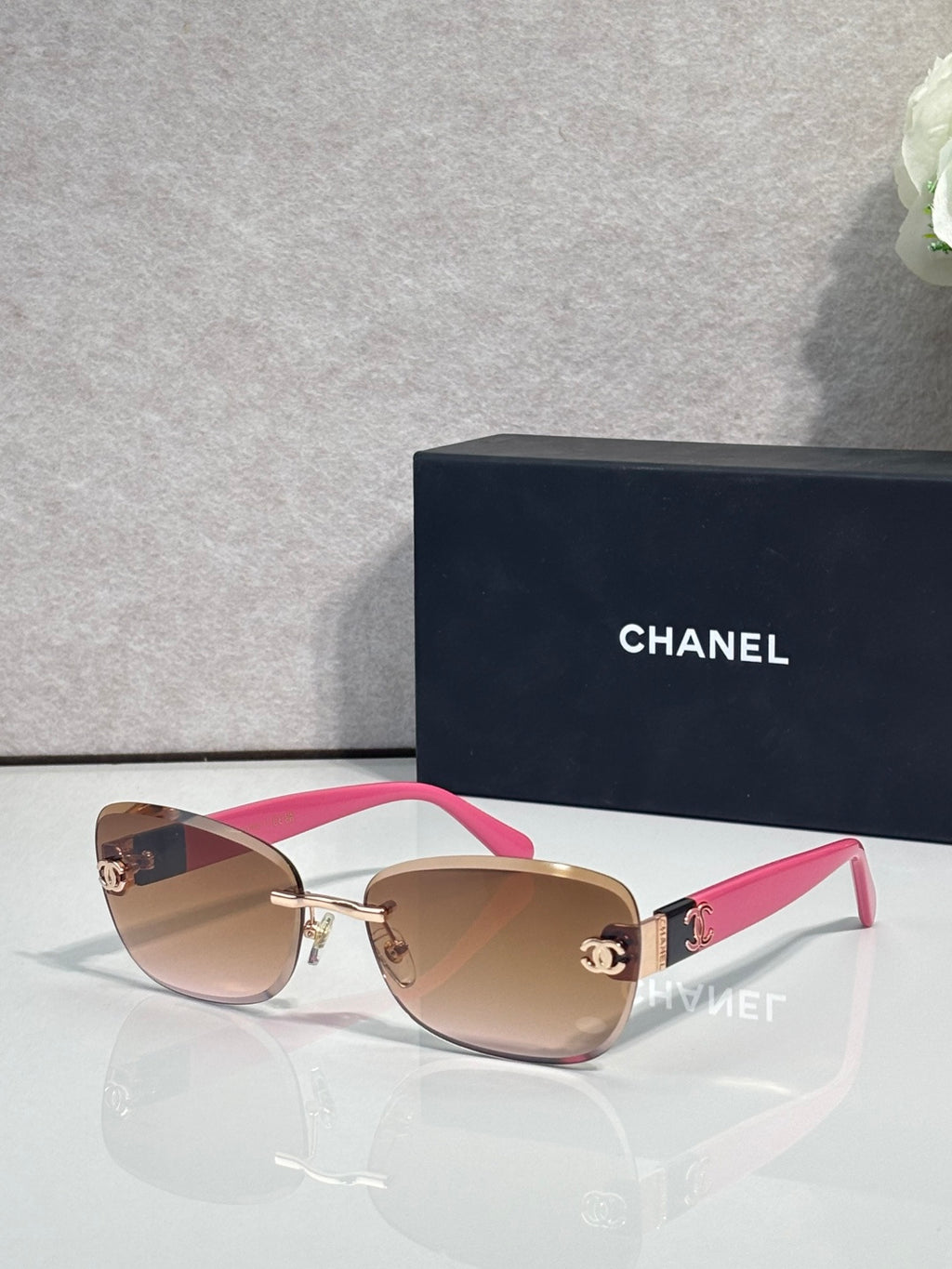 Sunglasses with white and pink frames, gold logo details, and pink tinted lenses