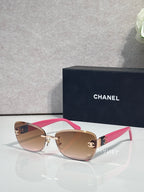 Sunglasses with white and pink frames, gold logo details, and pink tinted lenses