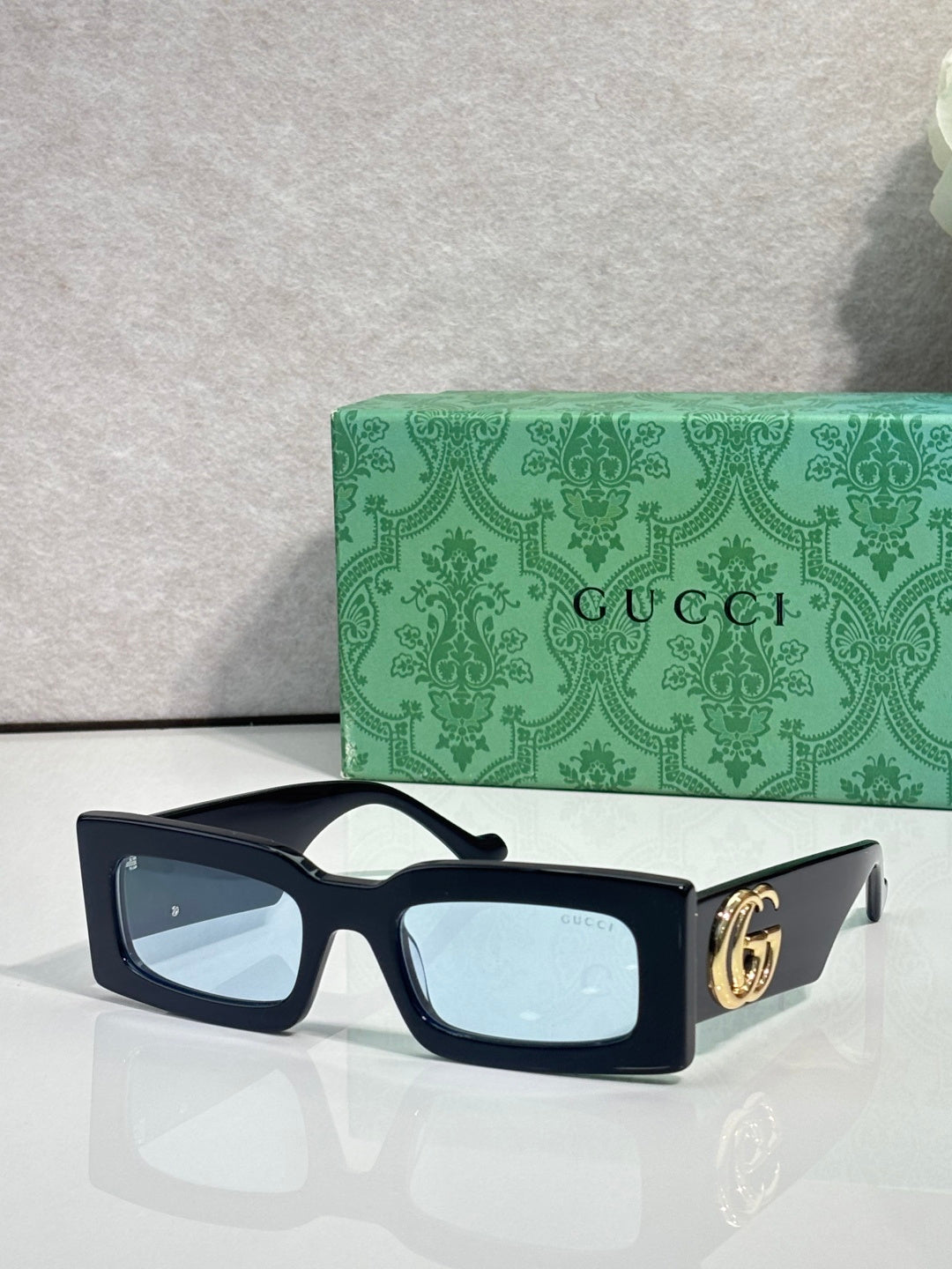 Rectangular dark sunglasses with light blue lenses and gold GG logo on temple