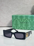 Rectangular black sunglasses with dark lenses and gold logo detail on arm