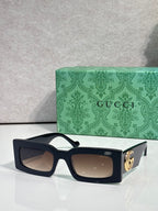Rectangular black sunglasses with brown lenses and gold logo on temple