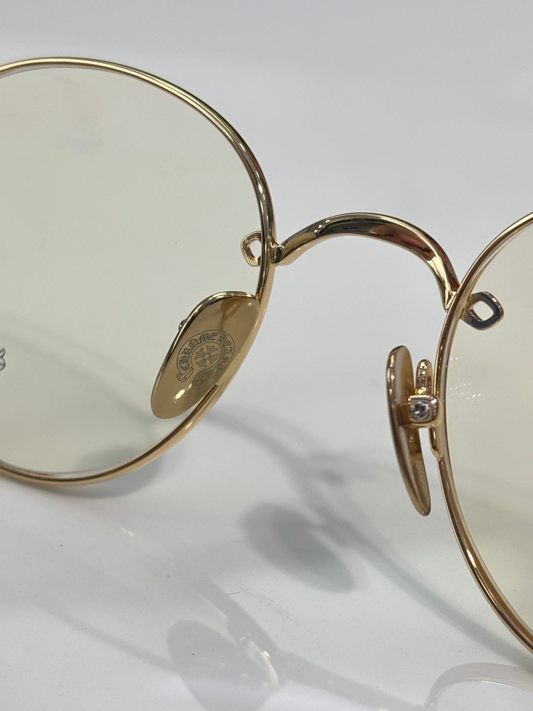 Metal eyeglass frame close-up with gold bridge and oval logo plate