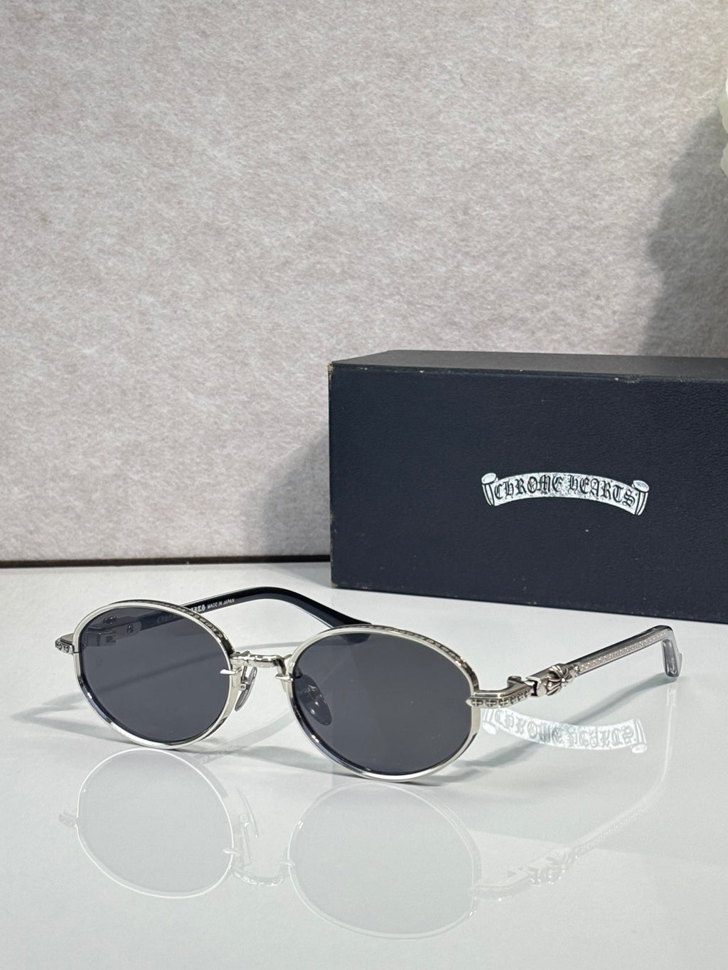 Chrome glasses with round dark lenses and black frames, gold-tone hinge detail.