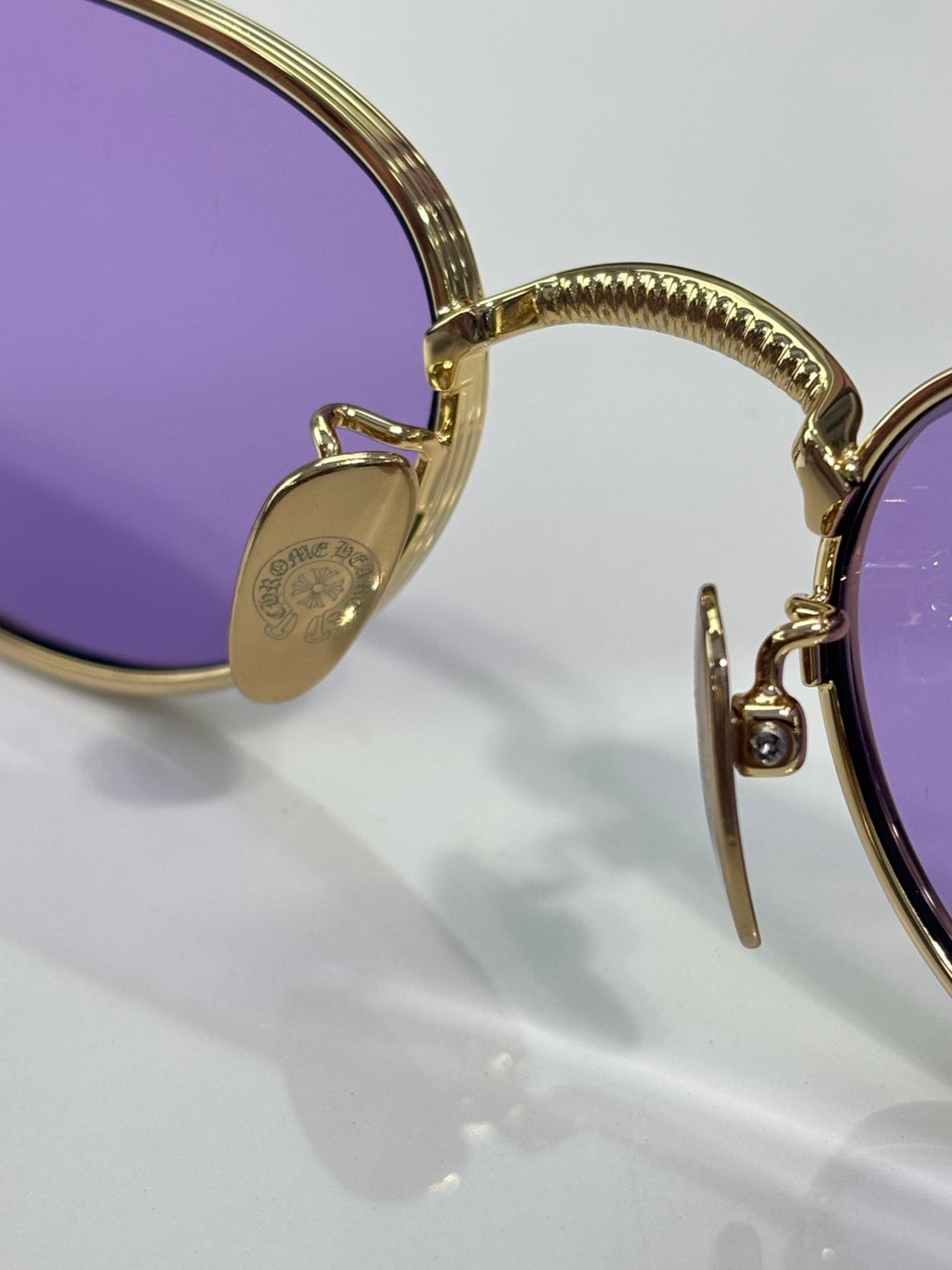 Close-up of gold sunglasses frame with purple lenses and hinged temple detail