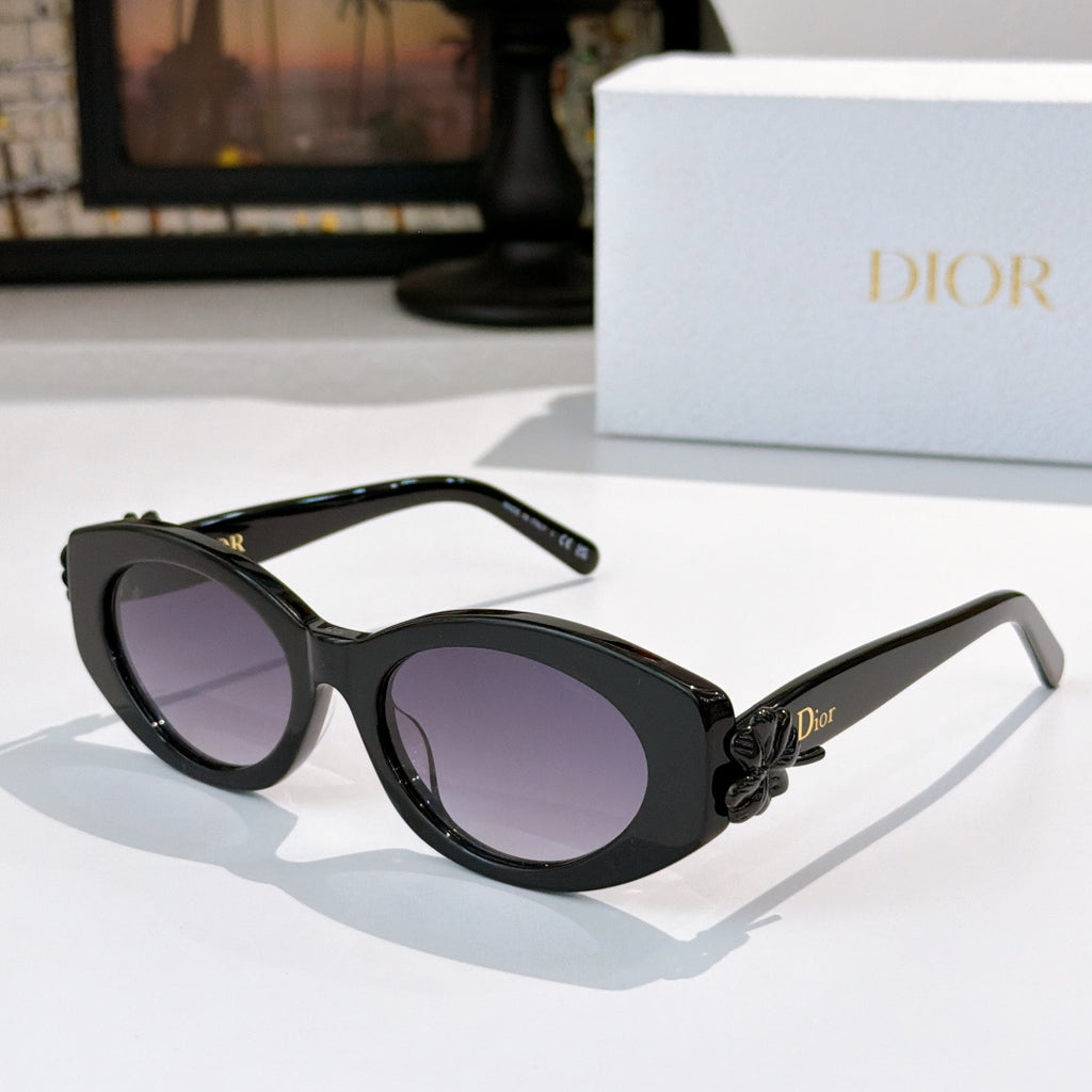 Dior sunglasses with black frames and purple-tinted lenses, with a small bow detail on the side.